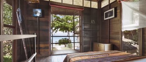 Un dormitorio de cabaña de madera con una cama, una ventana con vista a la playa y una mosquitera.