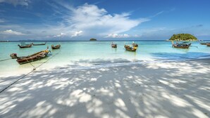A beach with several boats anchored near the shore, a sandy beach, and a small island in the distance. - Castaway Resort Koh Lipe (Koh Lipe)