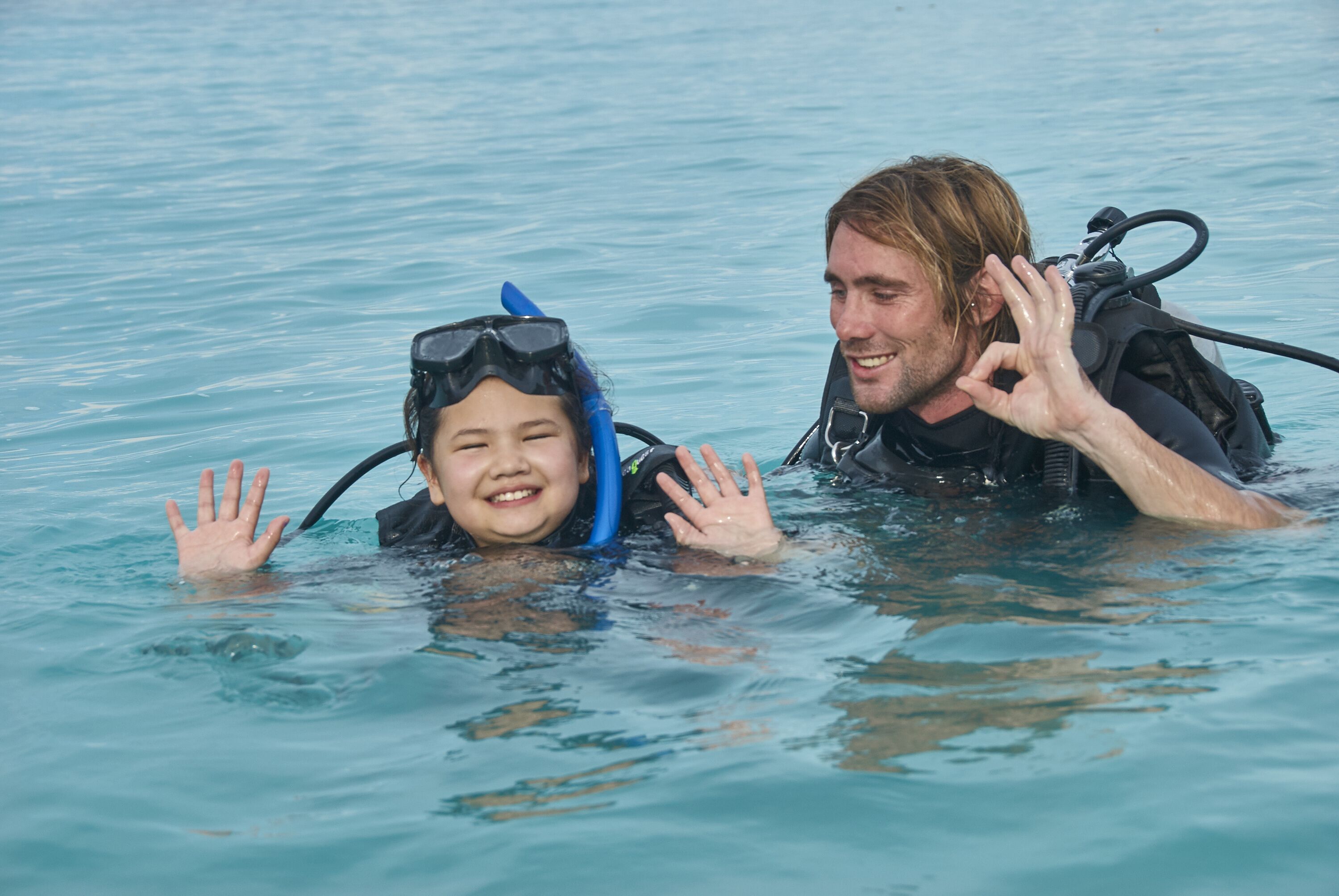 Two people in a body of water, one wearing a snorkel mask and the other with a scuba diving apparatus.