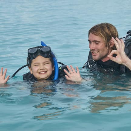 Two people in a body of water, one wearing a snorkel mask and the other with a scuba diving apparatus.