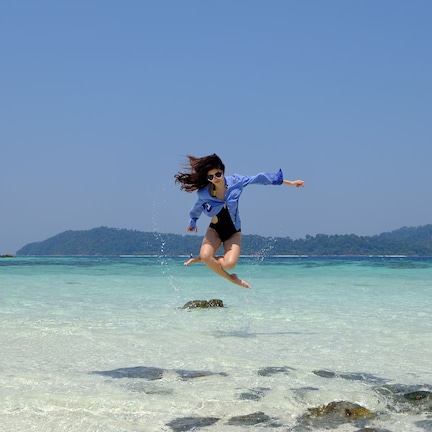 A person jumping into clear turquoise water with a rocky shore and green hills in the background.