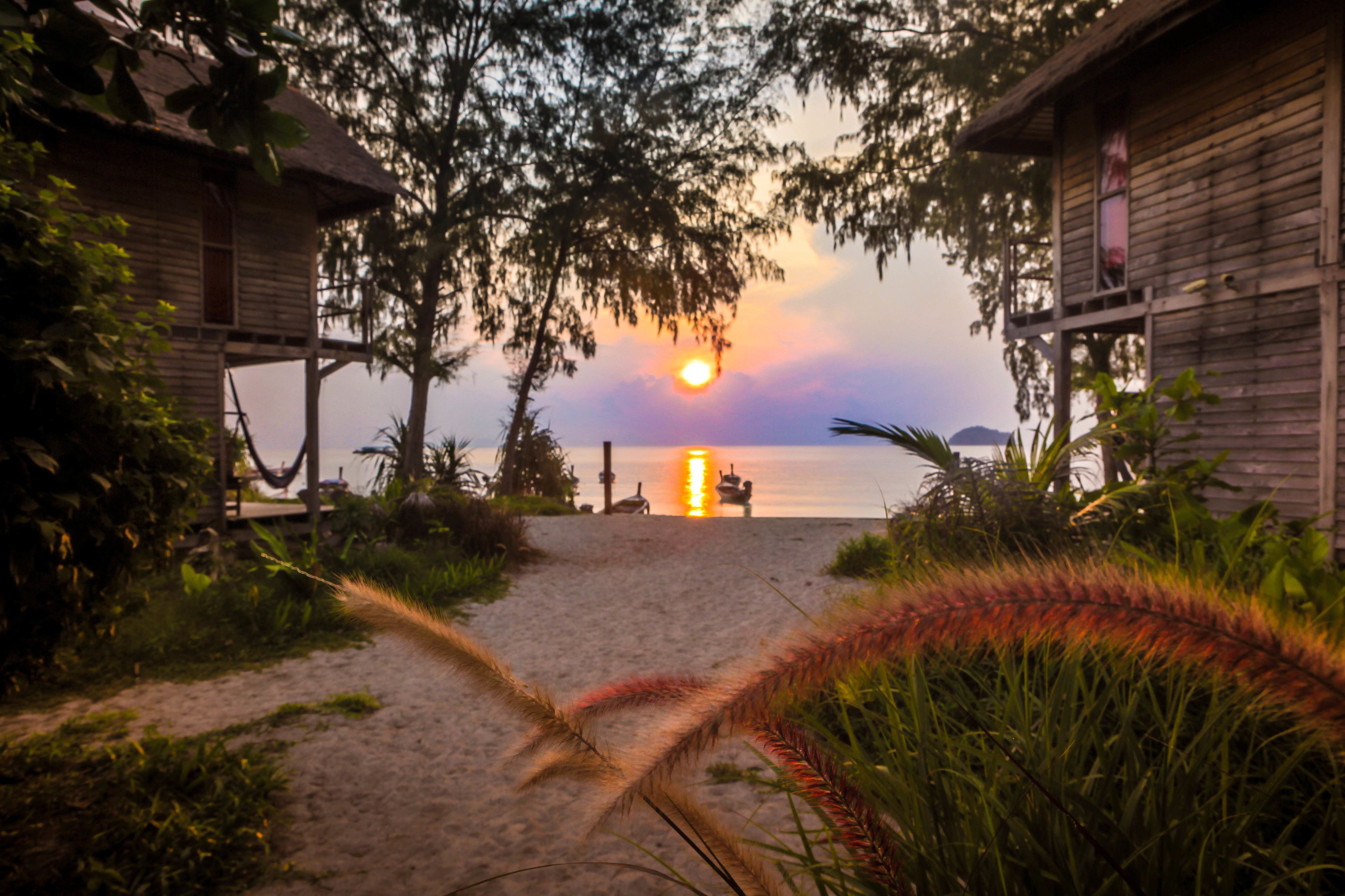 A beach path leading to a wooden structure with a view of the sunset over the water.