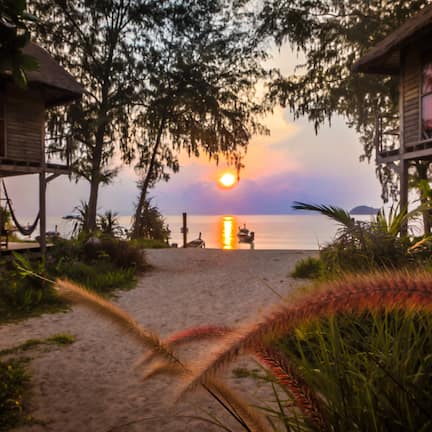 A beach path leading to a wooden structure with a view of the sunset over the water.
