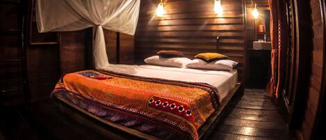 A room with a bed, a canopy, and a nightstand with a lamp.