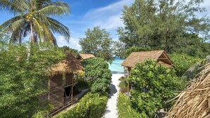 A pathway leading to a beach with thatched-roof huts surrounded by lush greenery and palm trees. - Castaway Resort Koh Lipe (Koh Lipe)