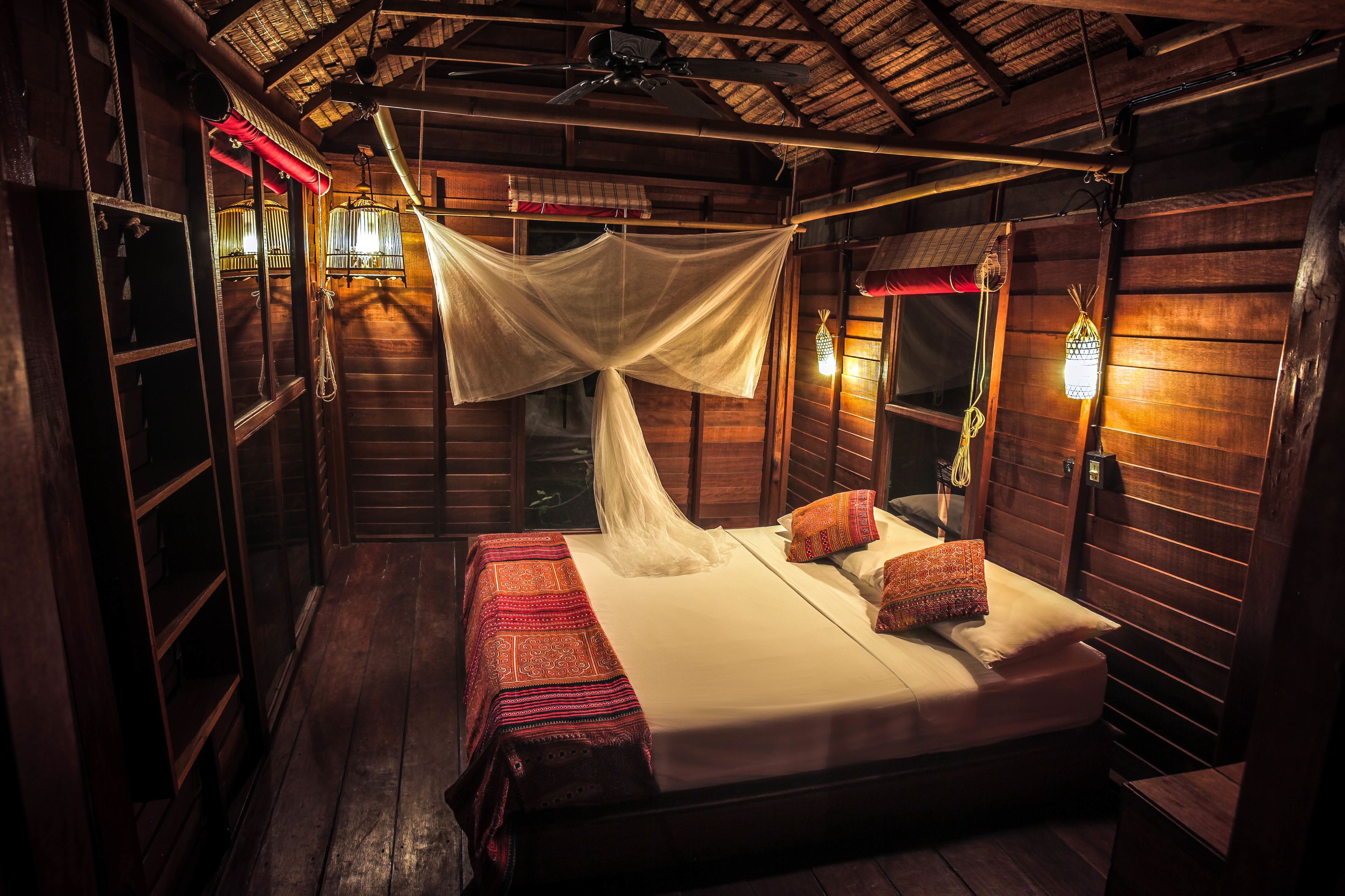 A wooden cabin room with a bed, mosquito net, and wall-mounted lights.