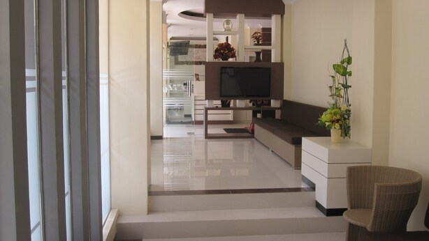 A modern living room with a flat-screen TV, a sofa, a wicker chair, and a small table with a vase of flowers. - Lily Guest House (Malang)