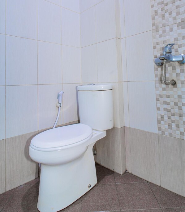 A white toilet with a bidet attachment in a bathroom with tiled walls and a shower area. - Lily Guest House (Malang)