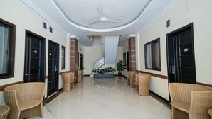 A hotel corridor with a ceiling fan, black doors, wicker chairs, and a staircase. - Lily Guest House (Malang)