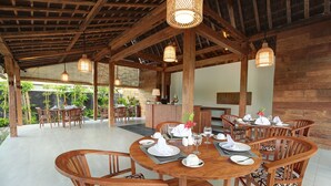Un comedor de madera con mesas y sillas redondas, una barra y vistas a palmeras.