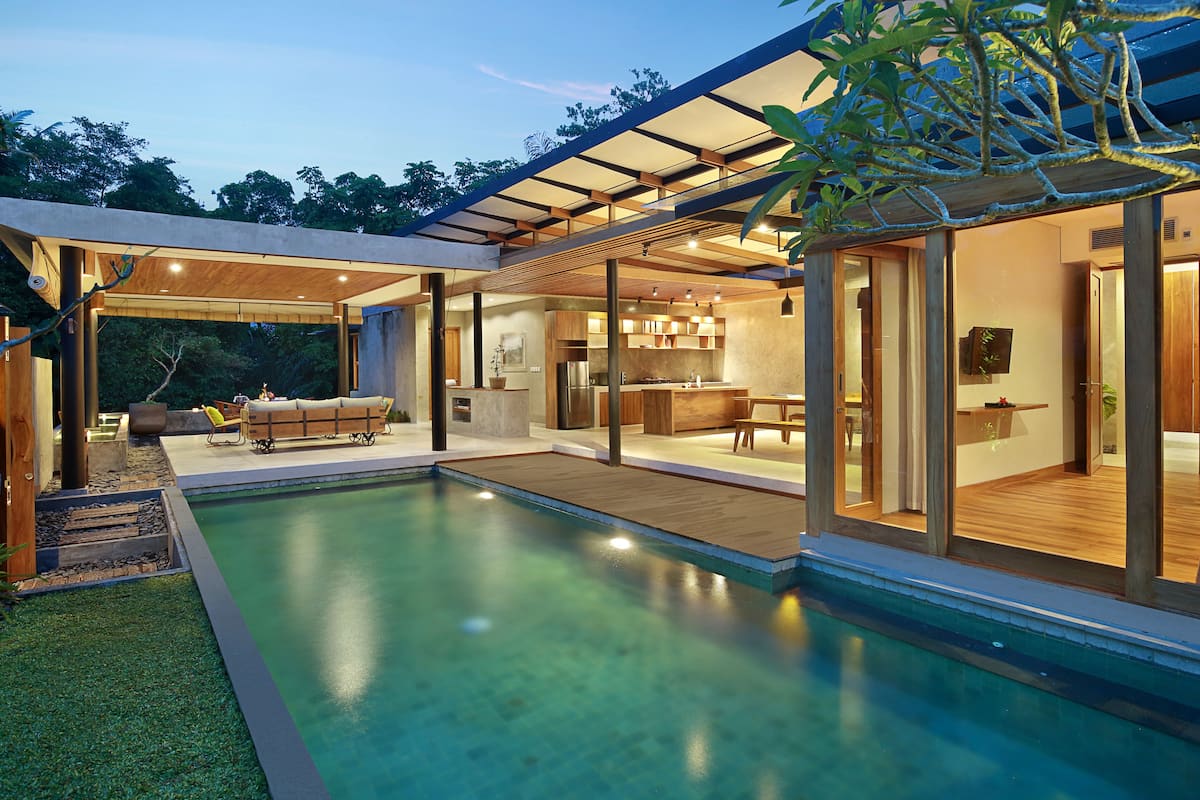 A modern house with a swimming pool, outdoor seating, and a kitchen visible through large glass doors.