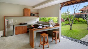 Una cocina moderna con una isla integrada, taburetes de madera, un refrigerador y vistas a un jardín exuberante.