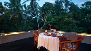 Un área de comedor al aire libre con una mesa dispuesta para dos, rodeada de exuberante vegetación y palmeras.