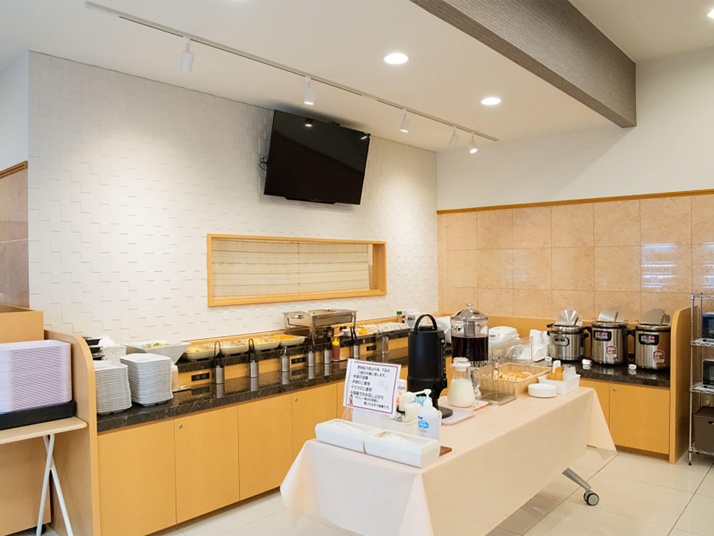 A modern breakfast bar with a flat-screen TV mounted on the wall, a variety of breakfast items, and a sign indicating the breakfast menu.