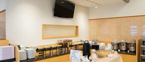 A modern breakfast bar with a flat-screen TV mounted on the wall, a variety of breakfast items, and a sign indicating the breakfast menu.