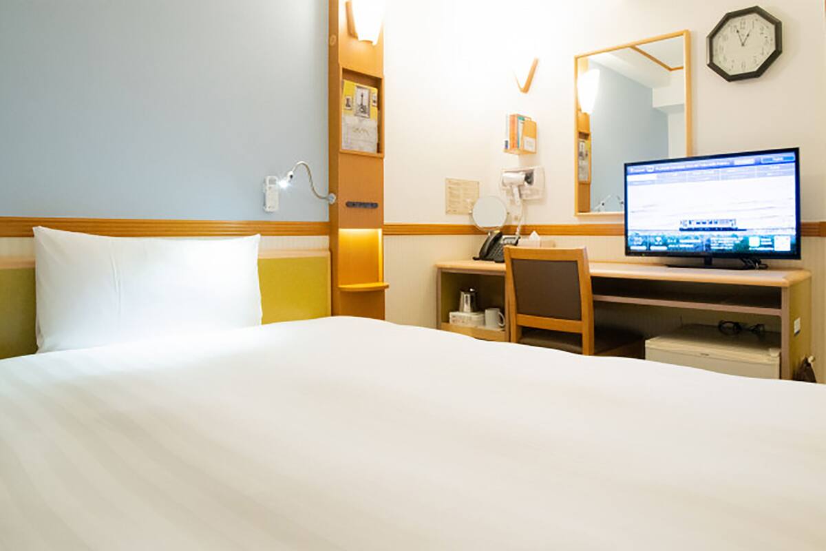 Habitación de hotel con cama, escritorio, silla, computadora, reloj y teléfono.