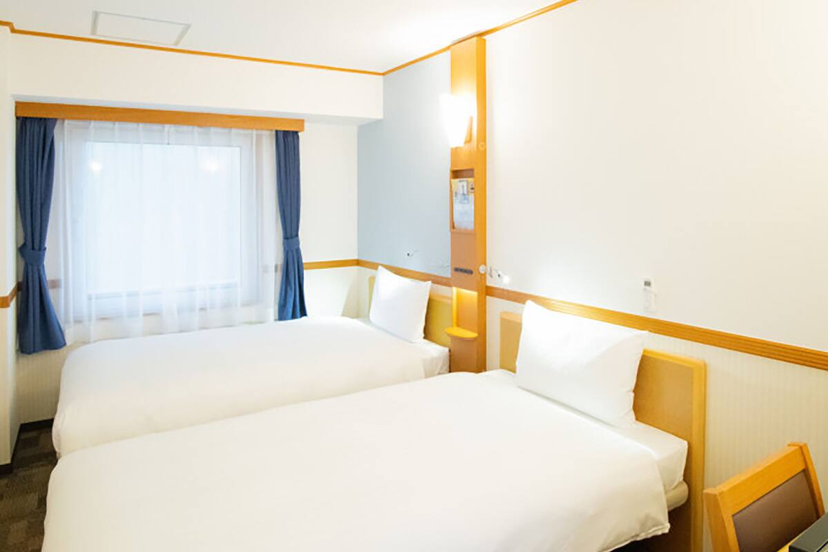 Habitación de hotel con dos camas, un ventanal con cortinas, una mesita de noche y un espejo.