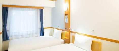 A hotel room with two beds, a large window with curtains, a bedside table, and a mirror.
