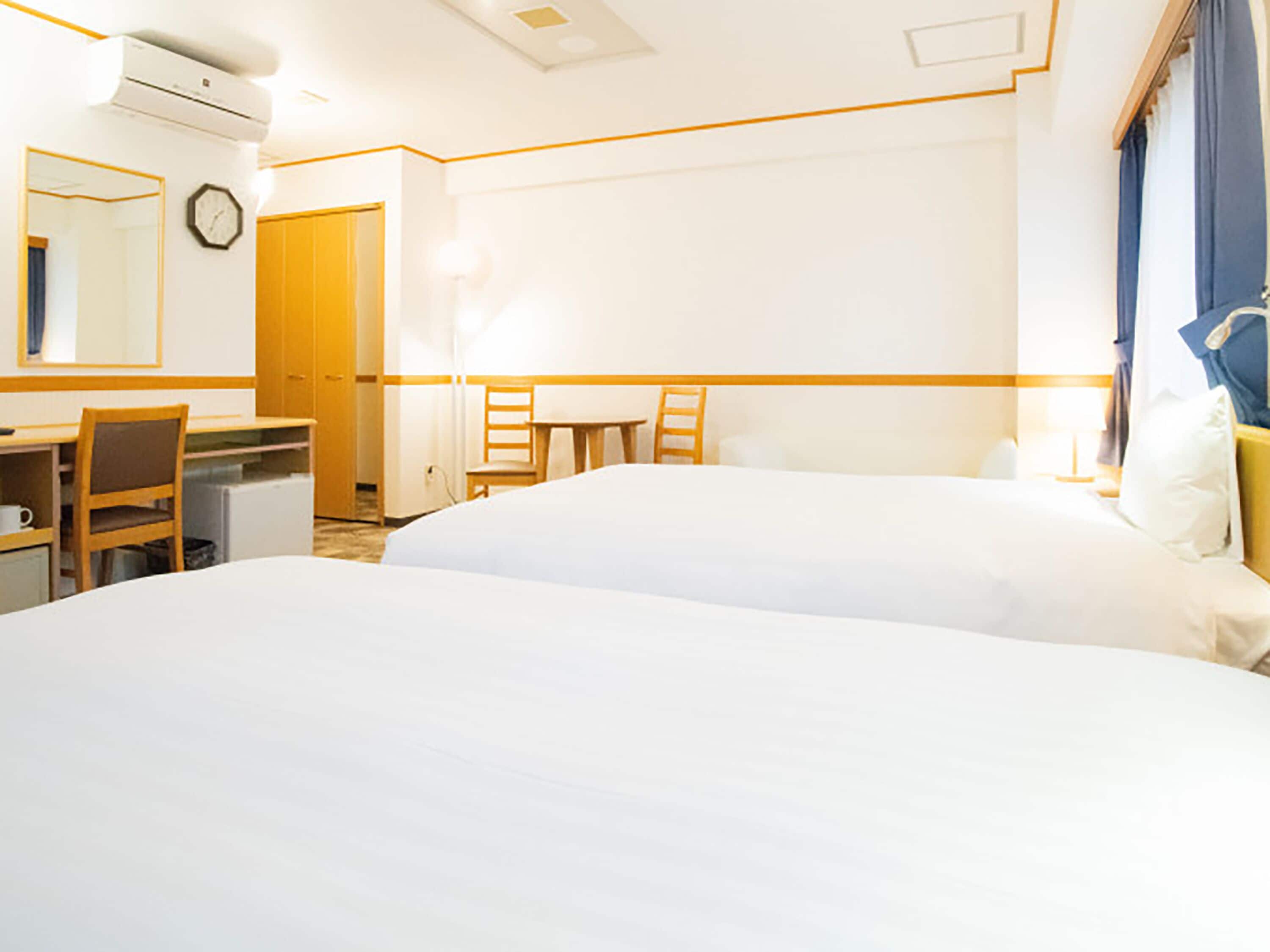 Habitación de hotel con dos camas, un escritorio, una silla, una mesita, un reloj y una ventana con cortinas.