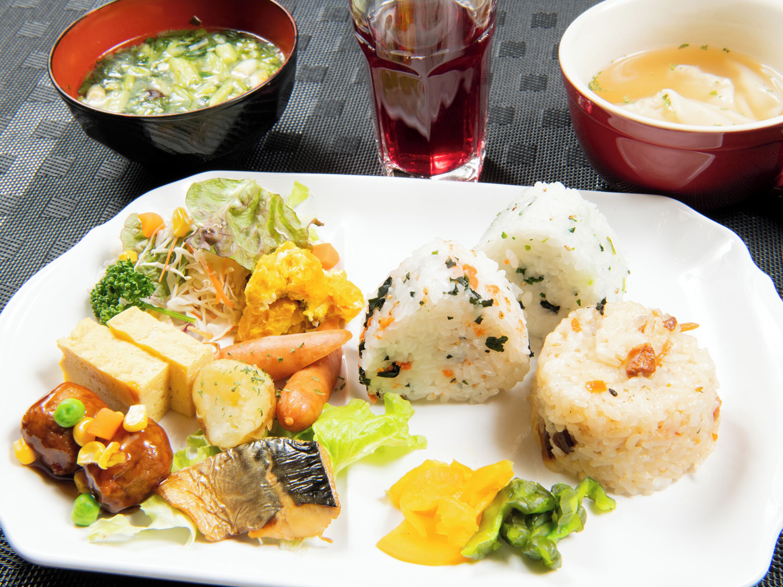 A plate of food with various dishes including rice, tofu, vegetables, and a soup bowl.