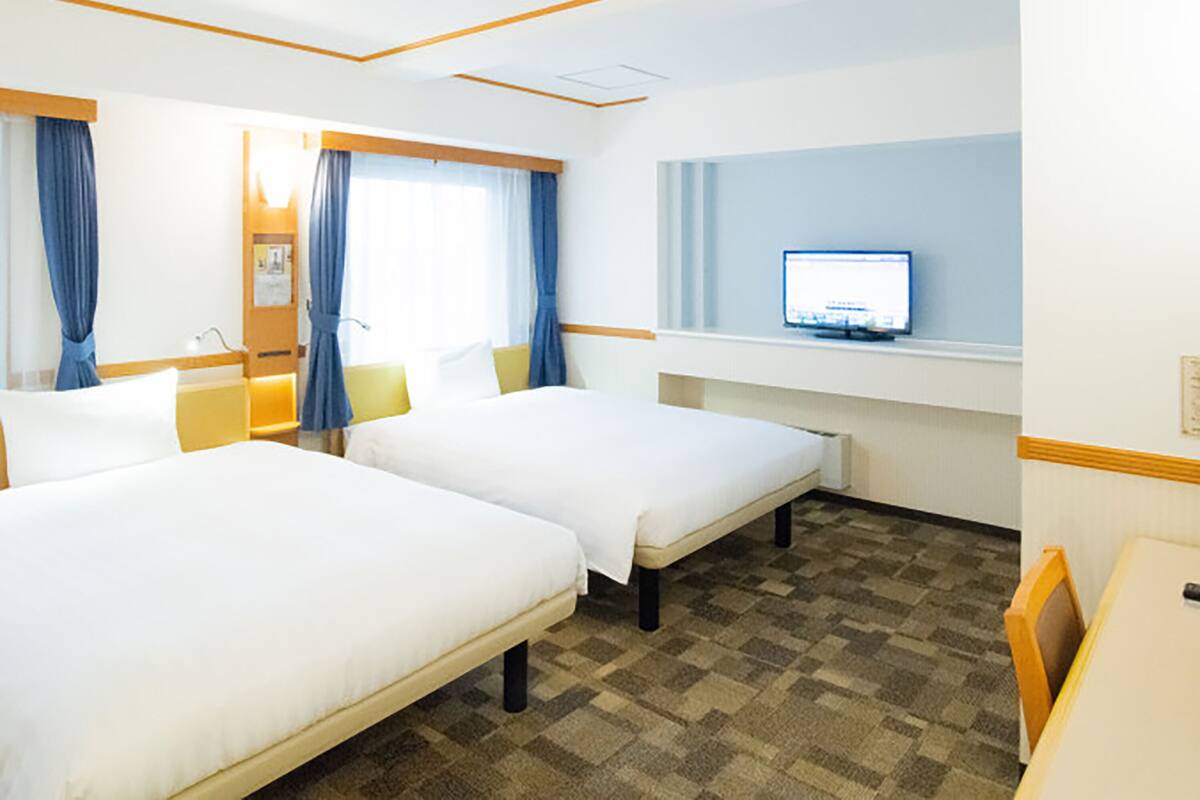 Habitación de hotel con dos camas, un escritorio, un televisor y una ventana con cortinas.