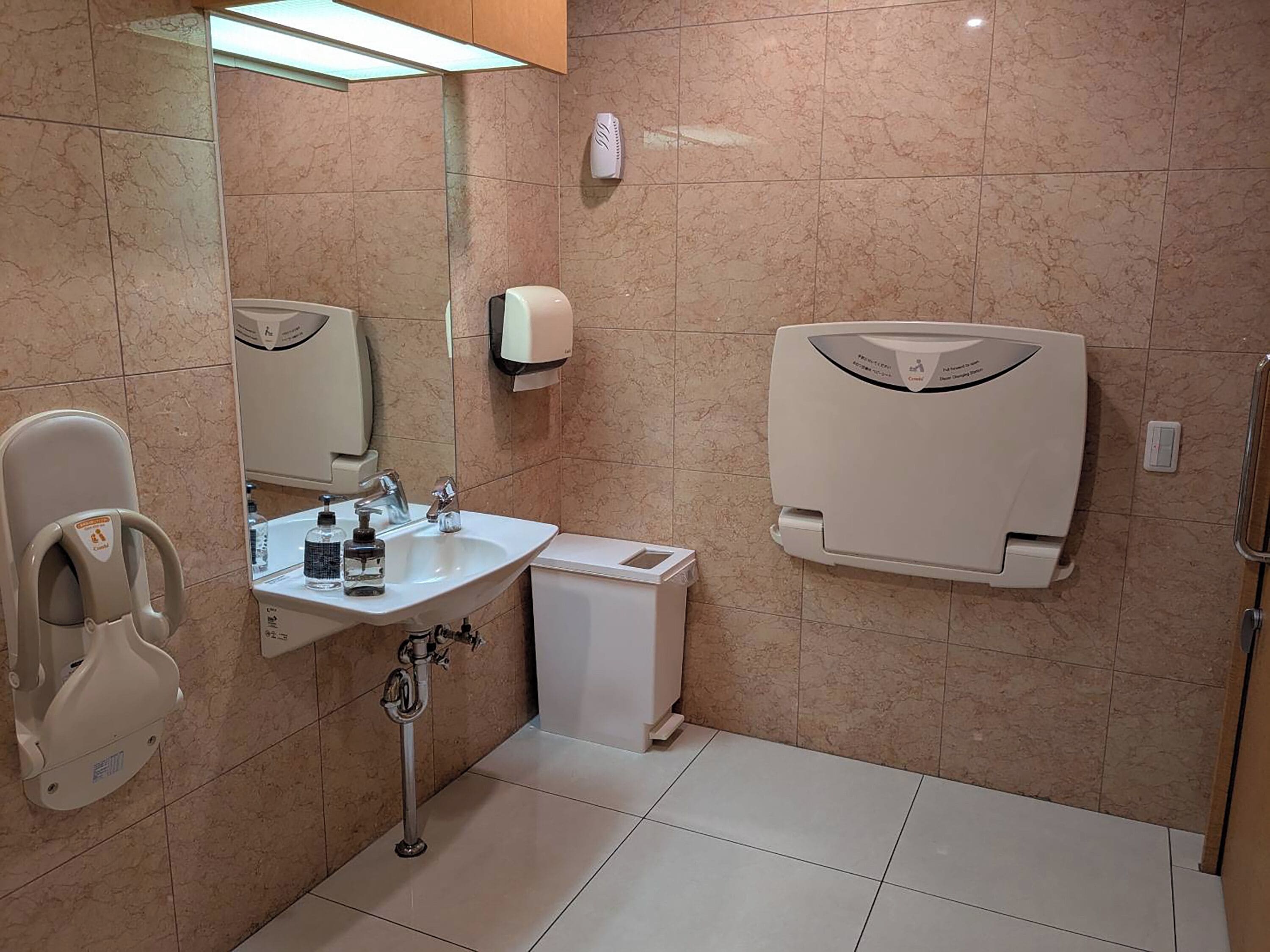 A modern bathroom with a sink, hand dryer, and a toilet with a safety rail.
