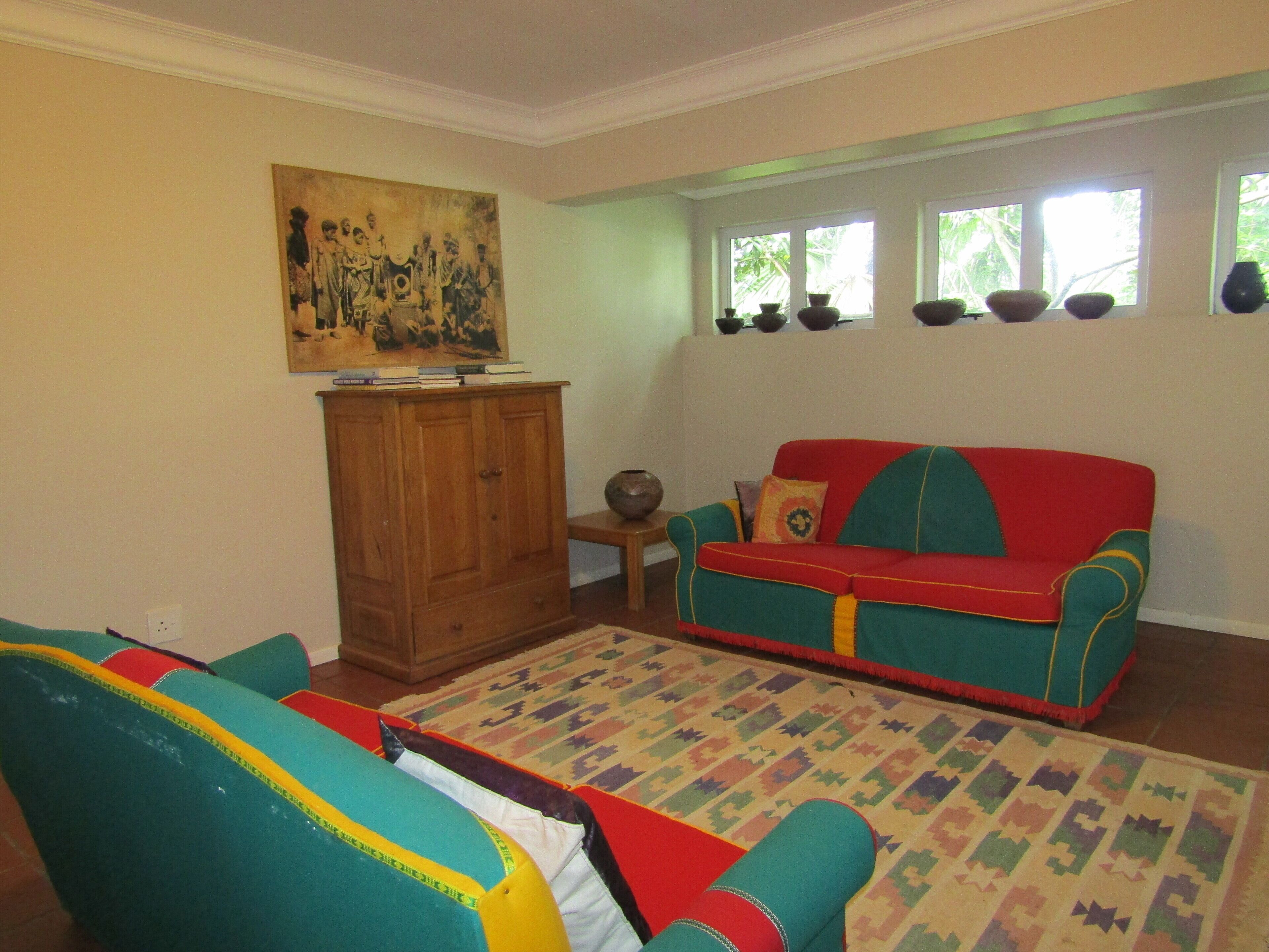 A living room with a colorful sofa, a wooden cabinet, and a painting on the wall.