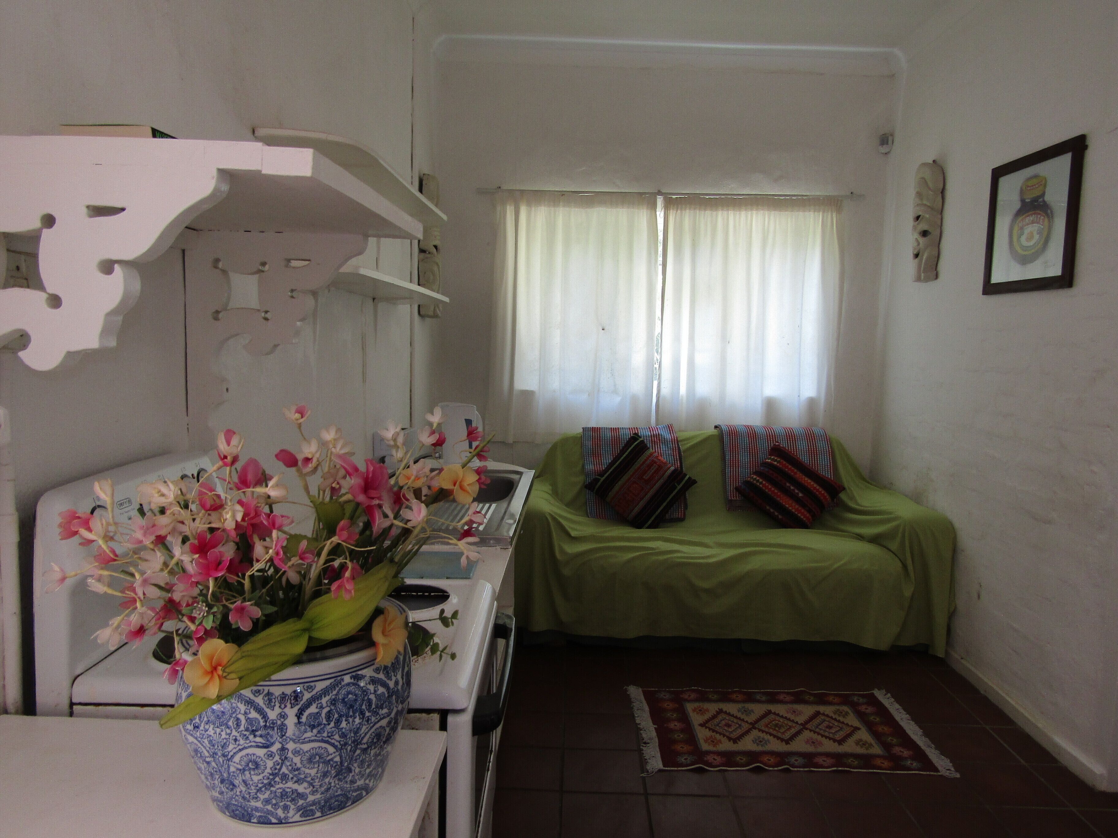 A room with a white stove, a green sofa with patterned cushions, a blue and white vase with flowers, and a patterned rug on the floor.