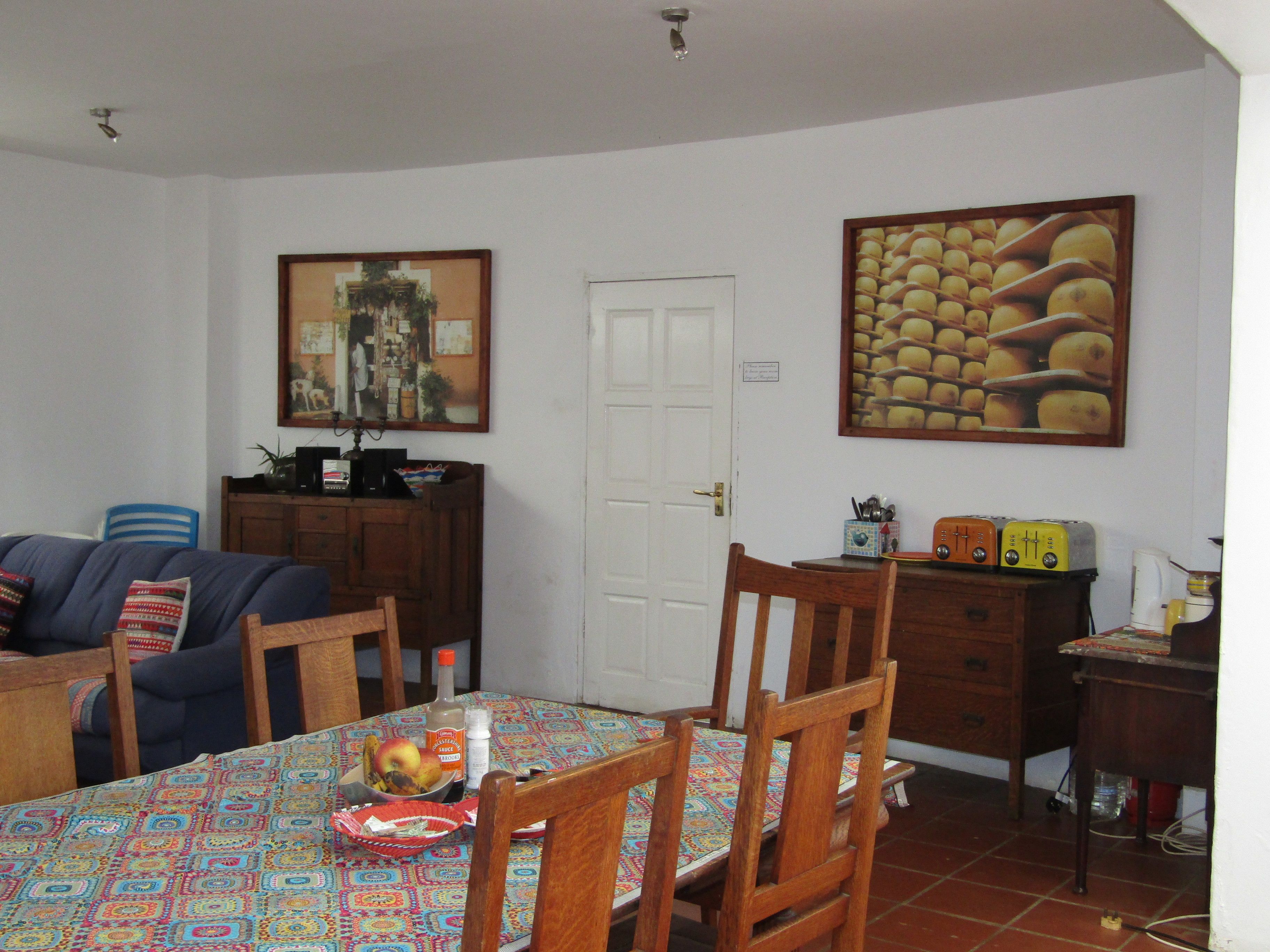 A dining area with a table set for four, surrounded by wooden chairs. A fruit bowl and condiments are on the table.