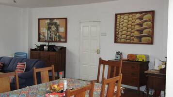 A dining area with a table set for four, surrounded by wooden chairs. A fruit bowl and condiments are on the table.