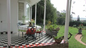 Une terrasse couverte avec un sol à carreaux, une table entourée de chaises et des plantes en pot.