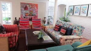 Un salon confortable avec un canapé, des fauteuils et une table basse. Il y a une grande fenêtre et une porte qui donne sur l’extérieur.