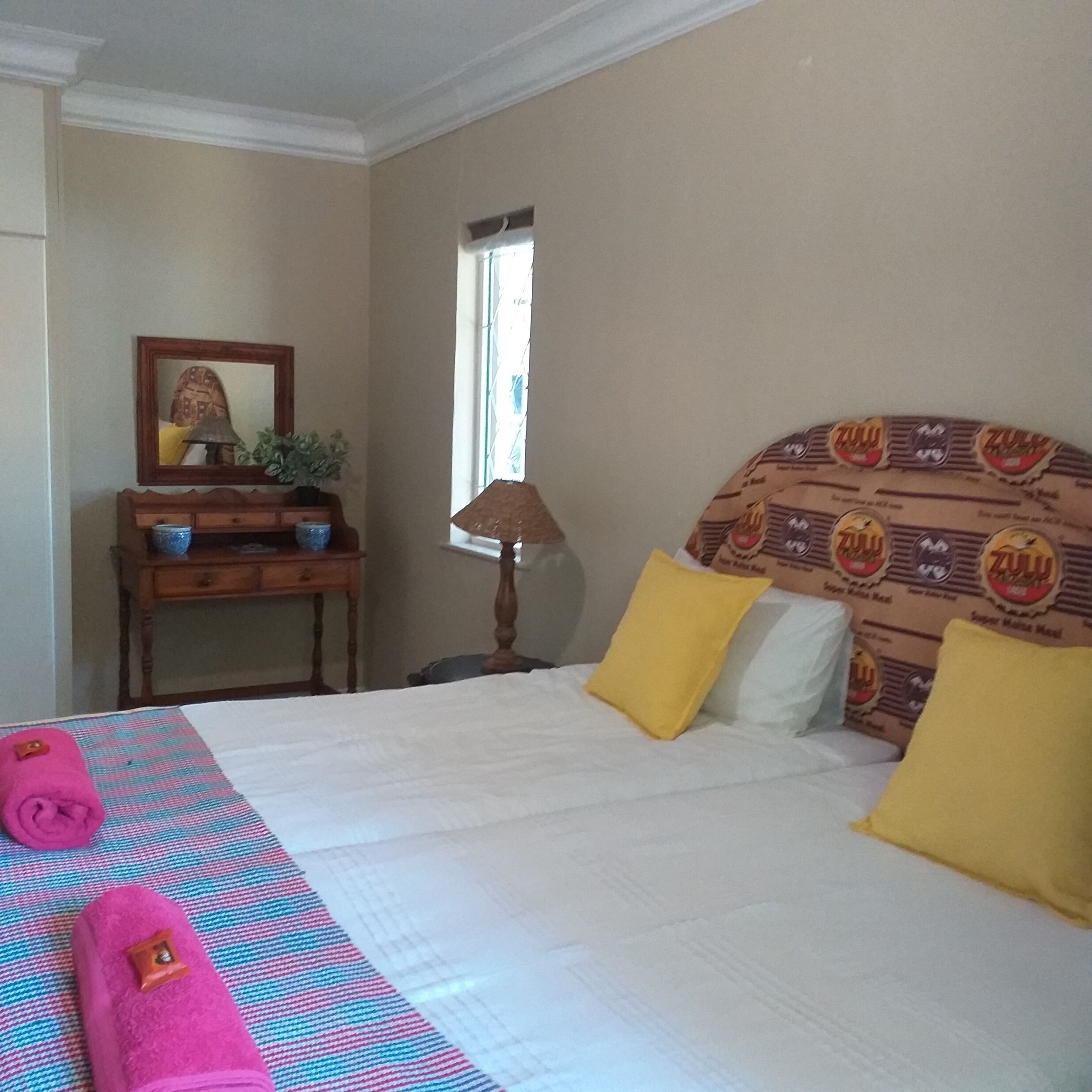 Hotelkamer met een bed, nachtkastje, lamp, raam en een wand met een gestreept hoofdeinde.