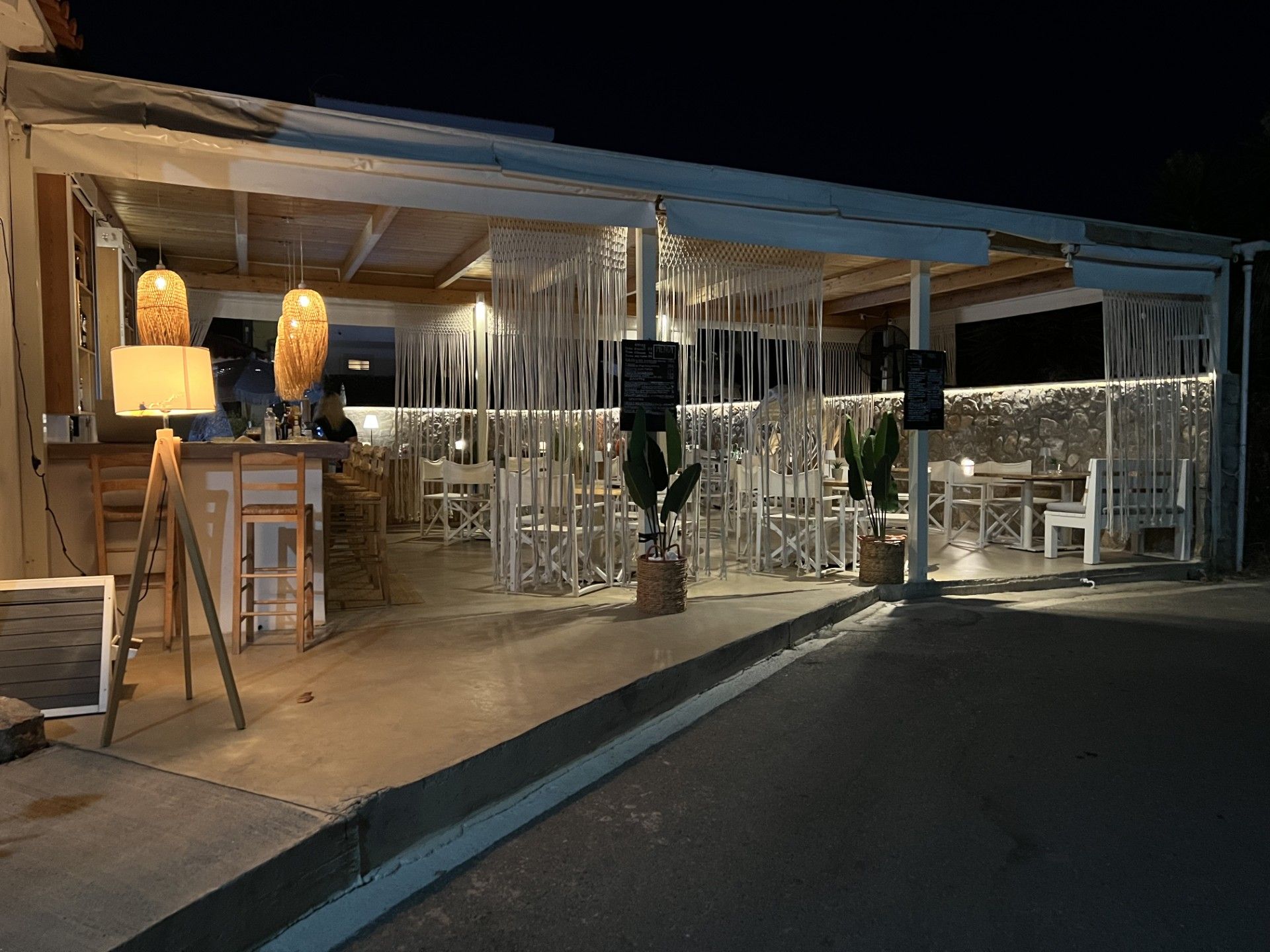 Zona d'estar a l'aire lliure amb taules i cadires, zona de bar amb barra, i un llum penjant decoratiu.