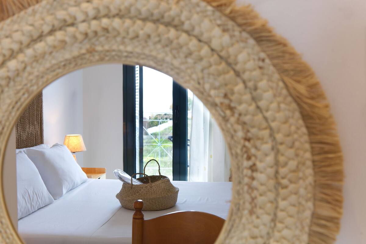 A bed with white linens, a wooden headboard, a bedside lamp, and a woven basket on the nightstand.