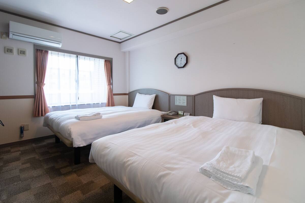 Een hotelkamer met twee bedden, een klok aan de muur en een airconditioner.
