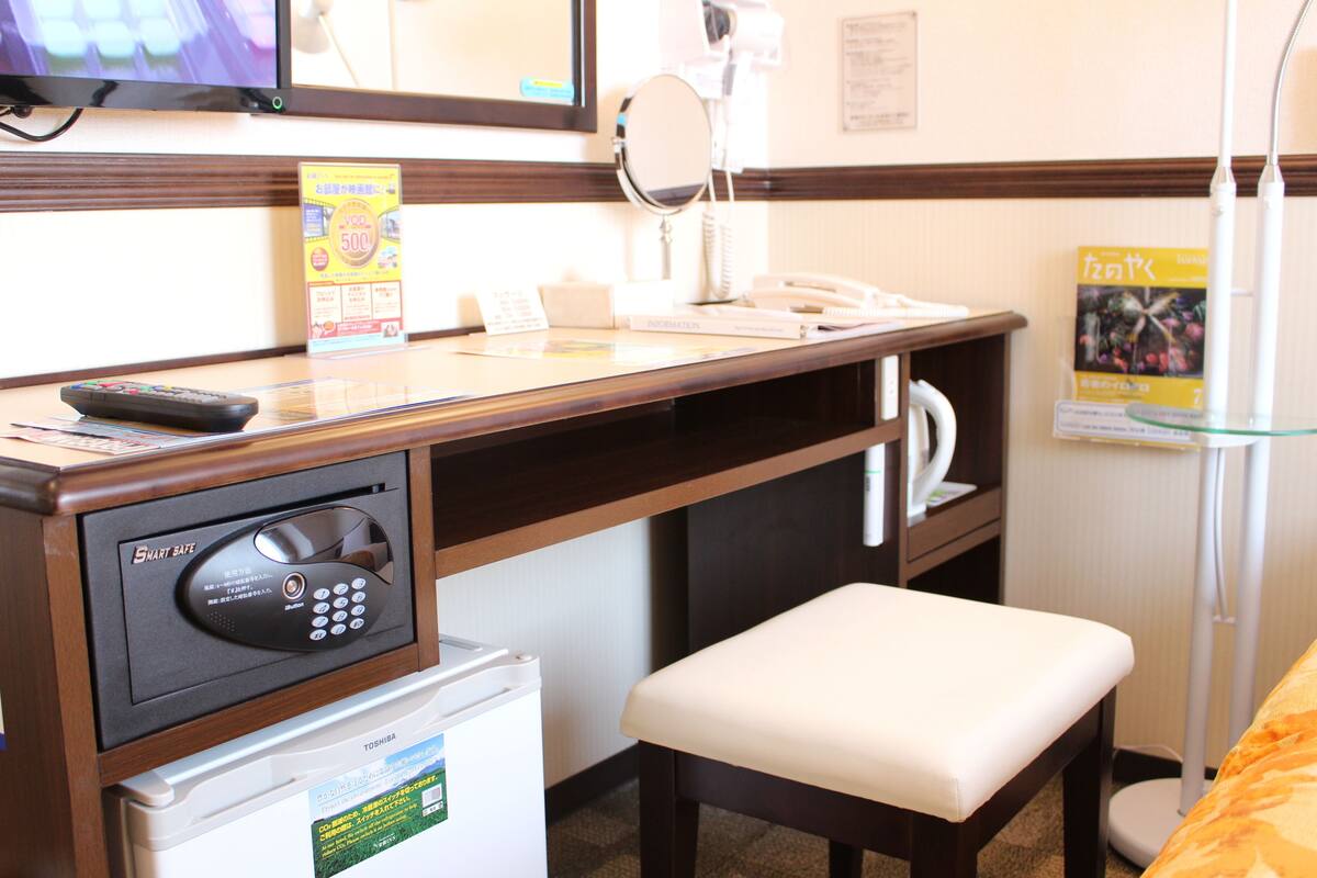 Hotelkamer met een bureau, een magnetron, een koelkast, een telefoon, een spiegel en een klein bankje.