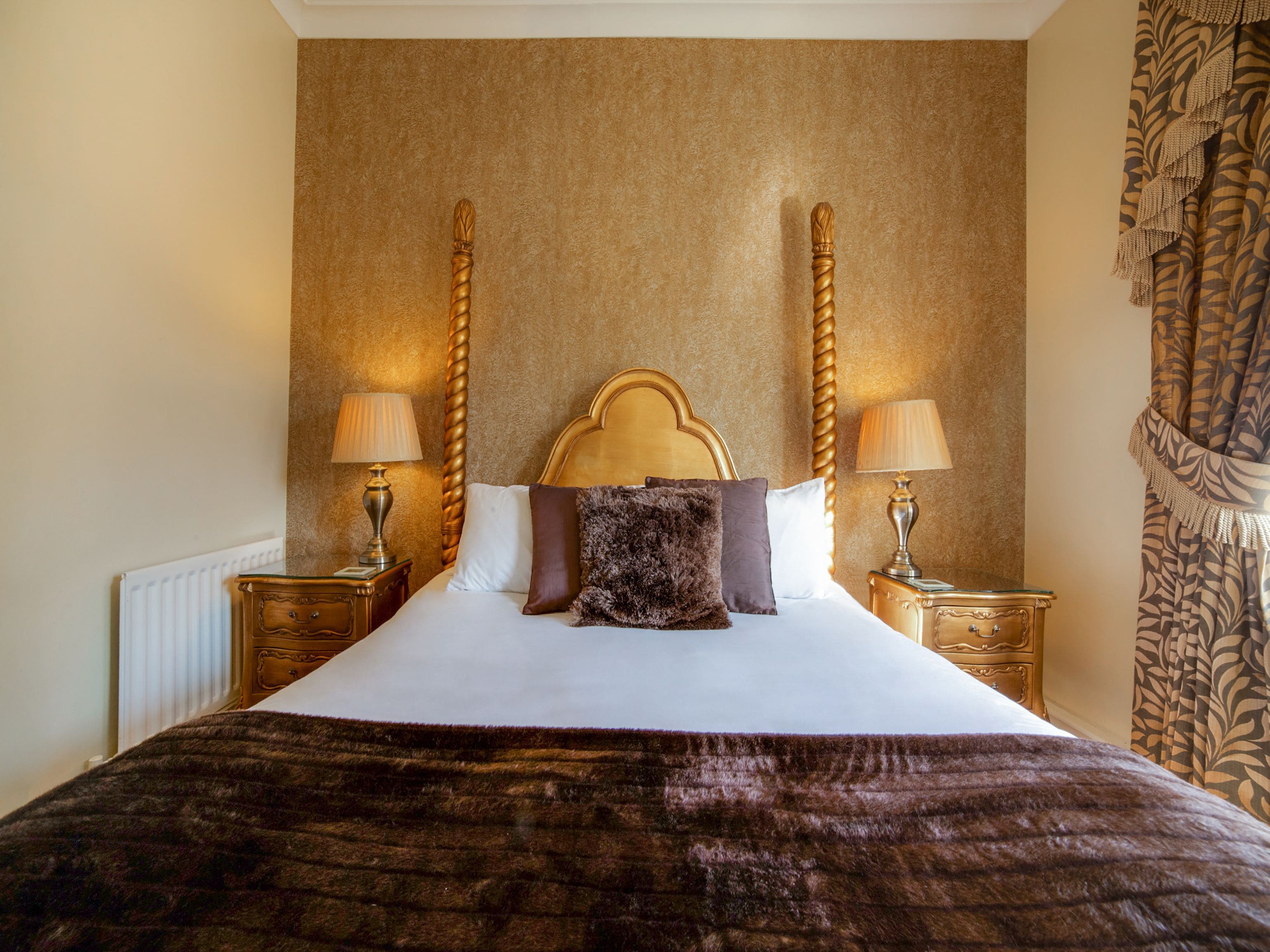 A large bed with a wooden headboard, two bedside tables with lamps, and a patterned curtain.