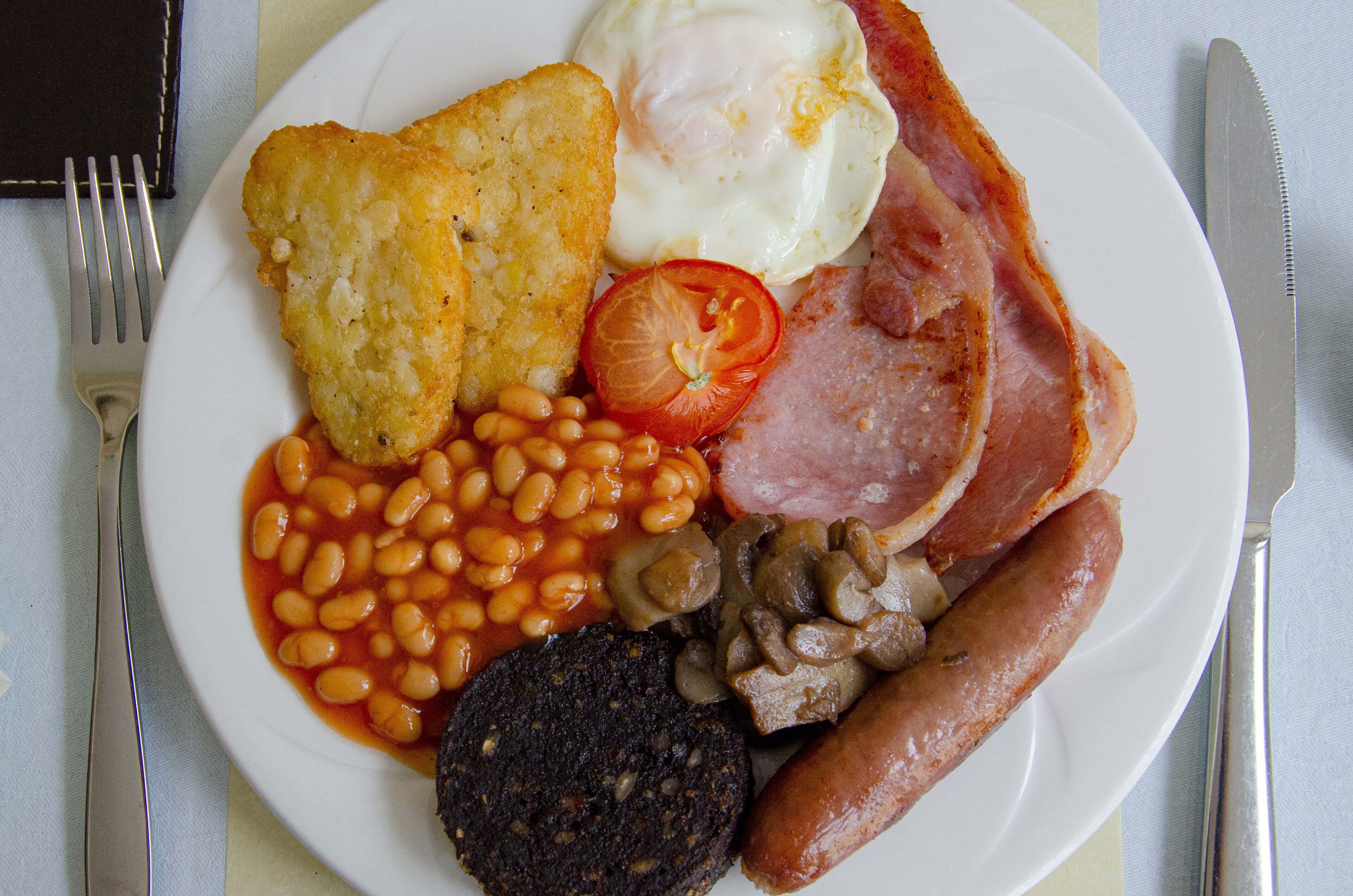 A plate of breakfast food including eggs, bacon, sausages, beans, and toast.
