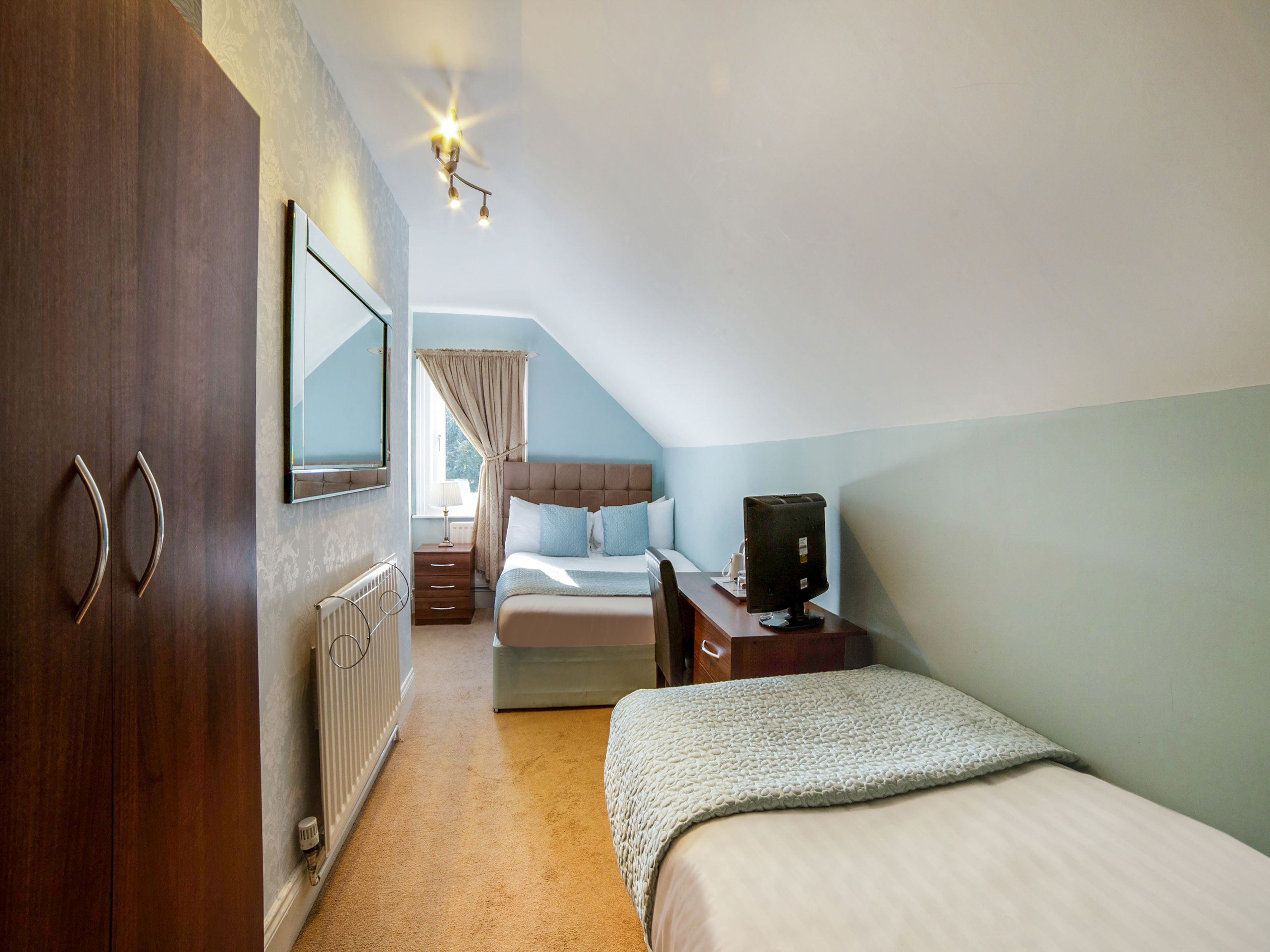 A bedroom with a bed, a desk with a computer, a wardrobe, and a radiator.