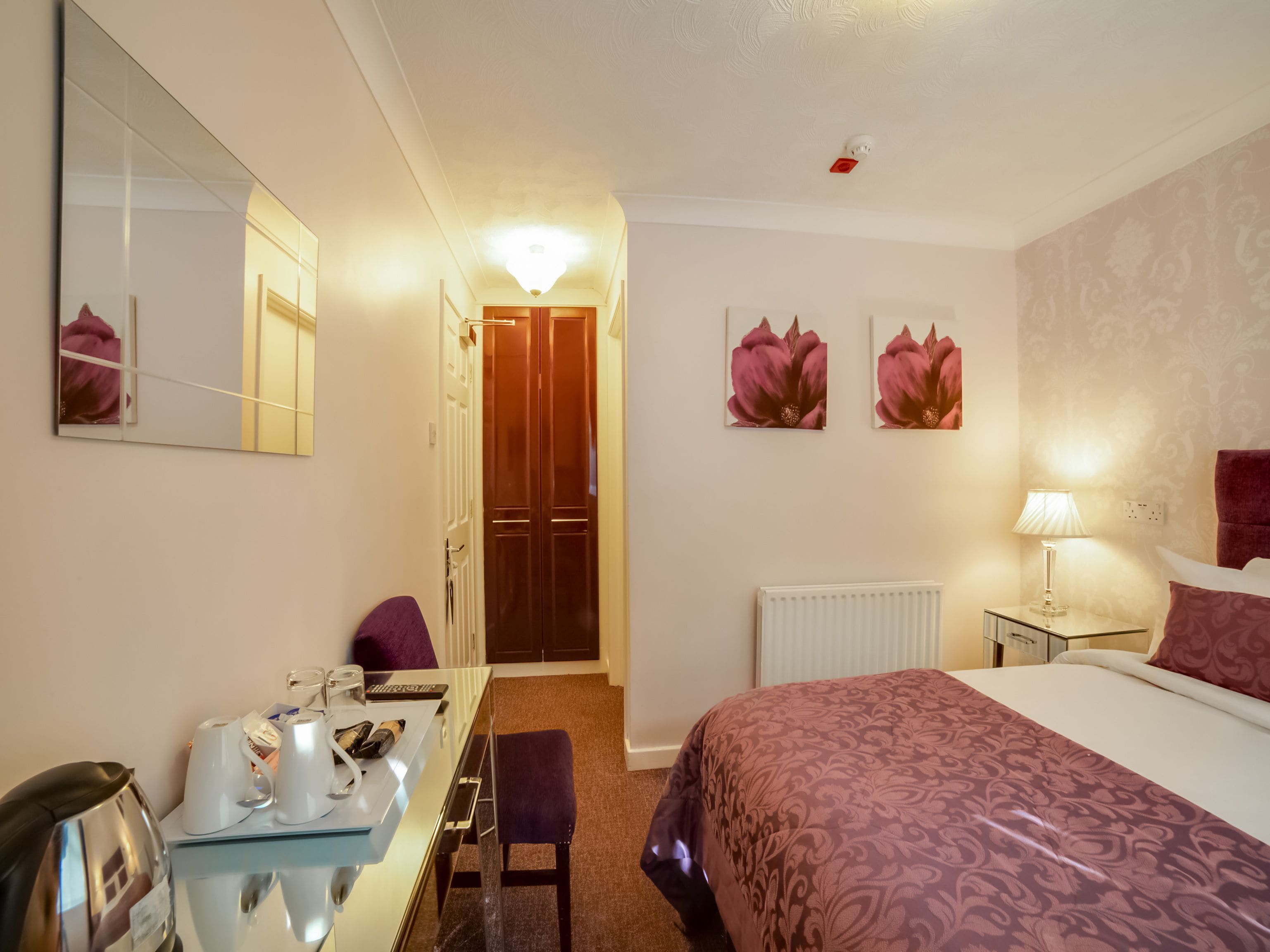 A hotel room with a bed, a desk with a chair, a mirror, and two wall-mounted flower paintings.