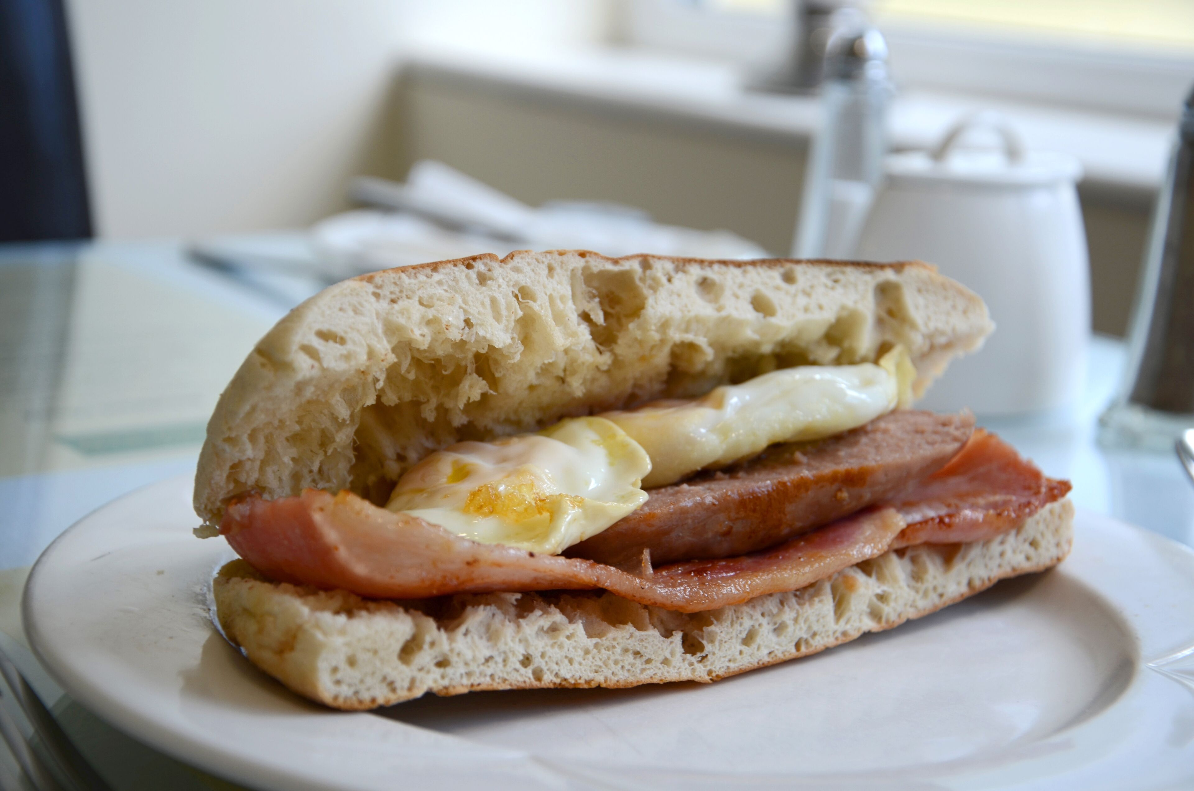 Un panino con uova e prosciutto su un piatto bianco.