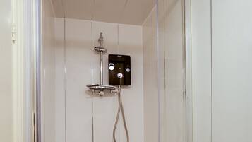 A small, enclosed shower area with a white tiled wall, a control panel, and a showerhead.