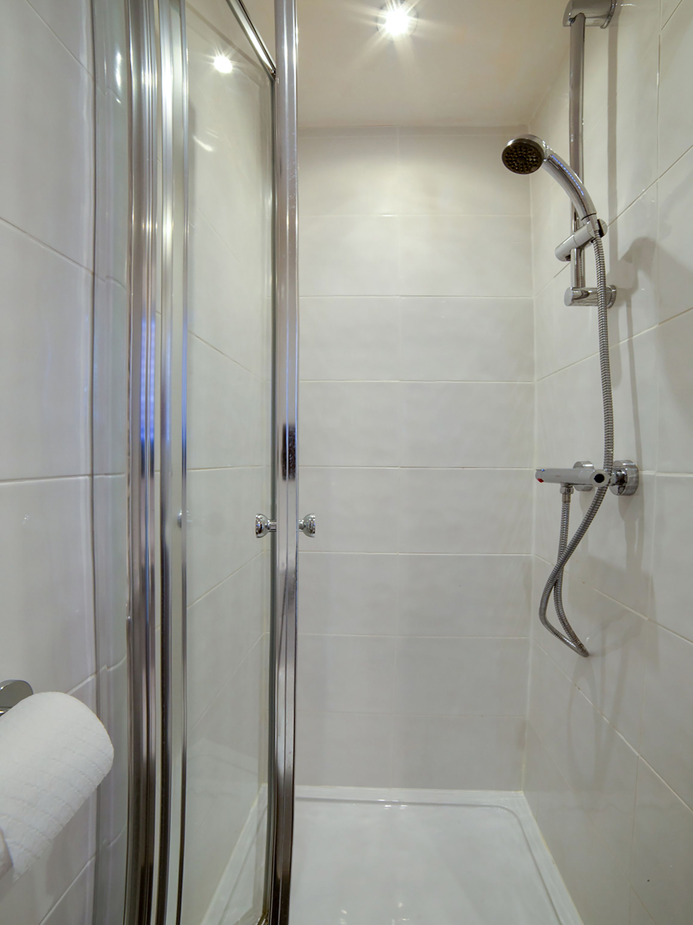 A modern shower area with a glass door, a handheld showerhead, and a wall-mounted faucet.
