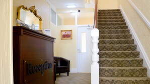 A reception area with a wooden desk labeled "Reception," a mirror, a framed picture, and a staircase with patterned carpet. - Lemonfield Hotel (Sunderland)