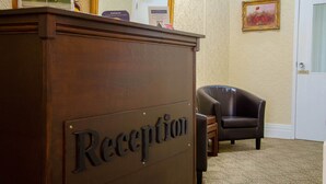 A reception desk labeled "Reception" with a sign above it, a framed picture on the wall, and a chair in the background. - Lemonfield Hotel (Sunderland)