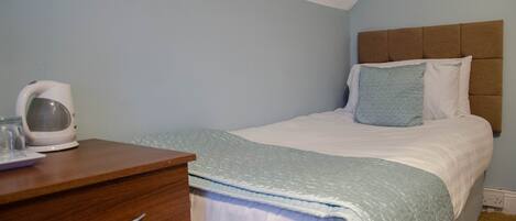 Un dormitorio con una cama, un aparador de madera y una tetera sobre el aparador.