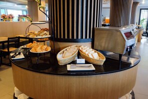 Een ontbijtbuffet met gebak, brood en een koffiehoek in een moderne hotelomgeving.