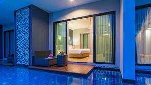 A modern hotel room with a large sliding glass door leading to a bedroom, a small outdoor seating area with a wicker chair and a table, and a poolside view. - Ava Sea Krabi Resort (Krabi)
