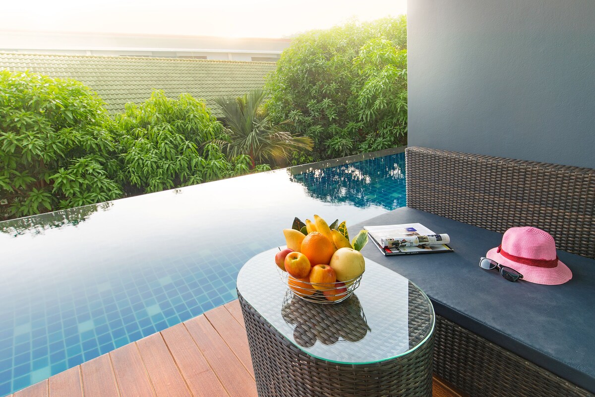A poolside area with a glass table holding a fruit bowl, sunglasses, and a hat.